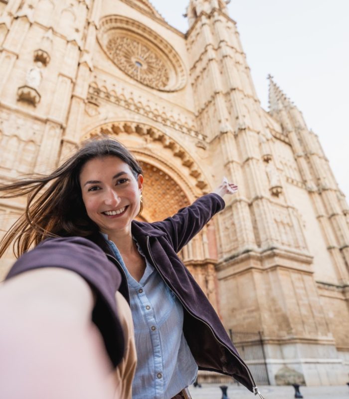 Smiling young woman taking a selfie in front of the historic palma cathedral